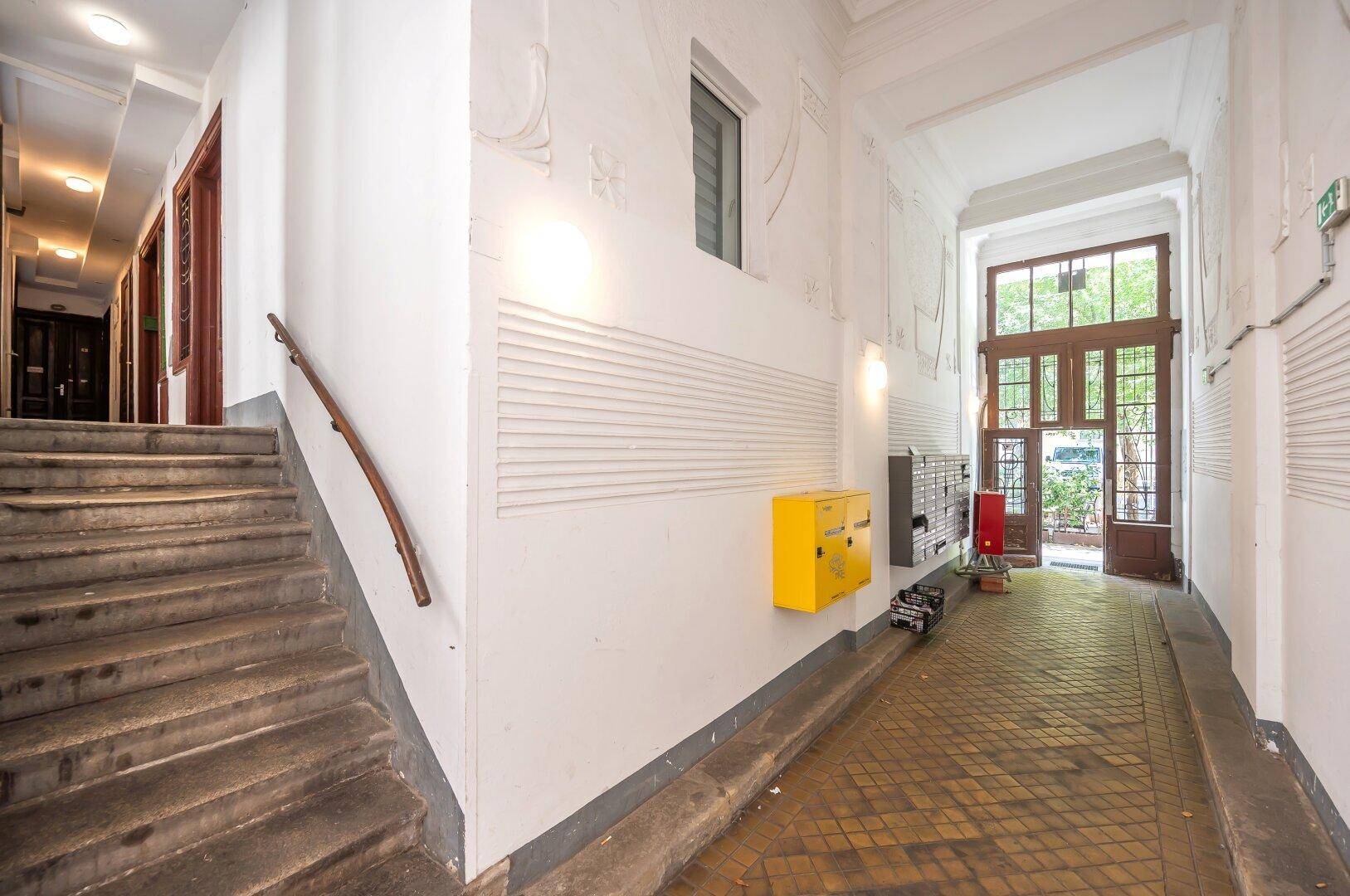 Geräumiger Eingangsbereich mit Treppe, Briefkästen und großen Holztüren zur Straße hin.