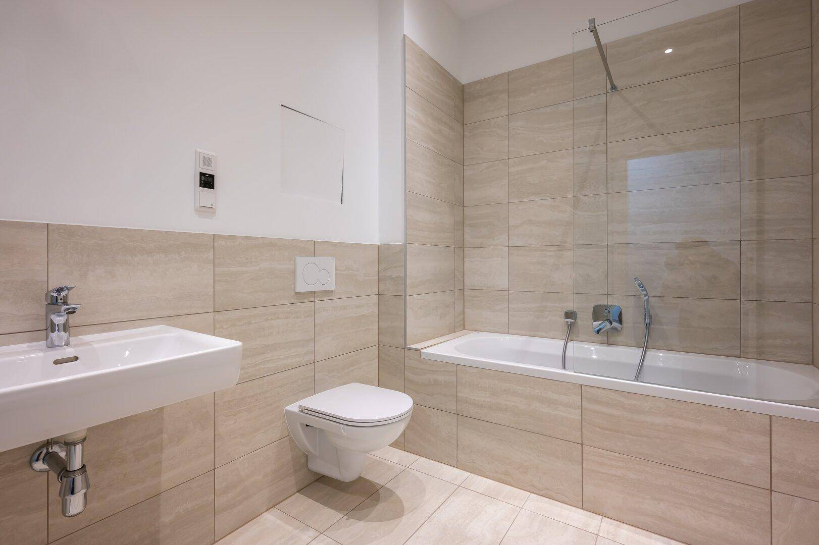 Helles Badezimmer mit Waschbecken, wandhängendem WC und integrierter Badewanne.