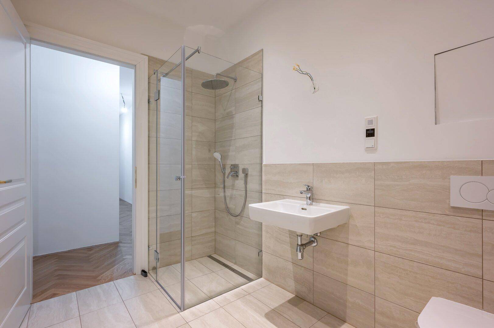 Helles Badezimmer mit moderner Glasdusche, Waschbecken und beigefarbenen Wandfliesen.