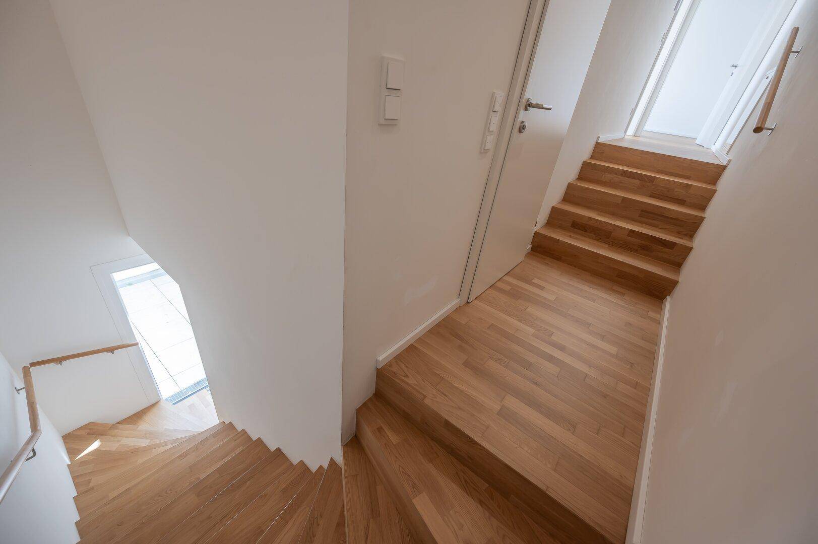 Holztreppe führt in die obere Etage, umgeben von hellen Wänden und Holzboden.