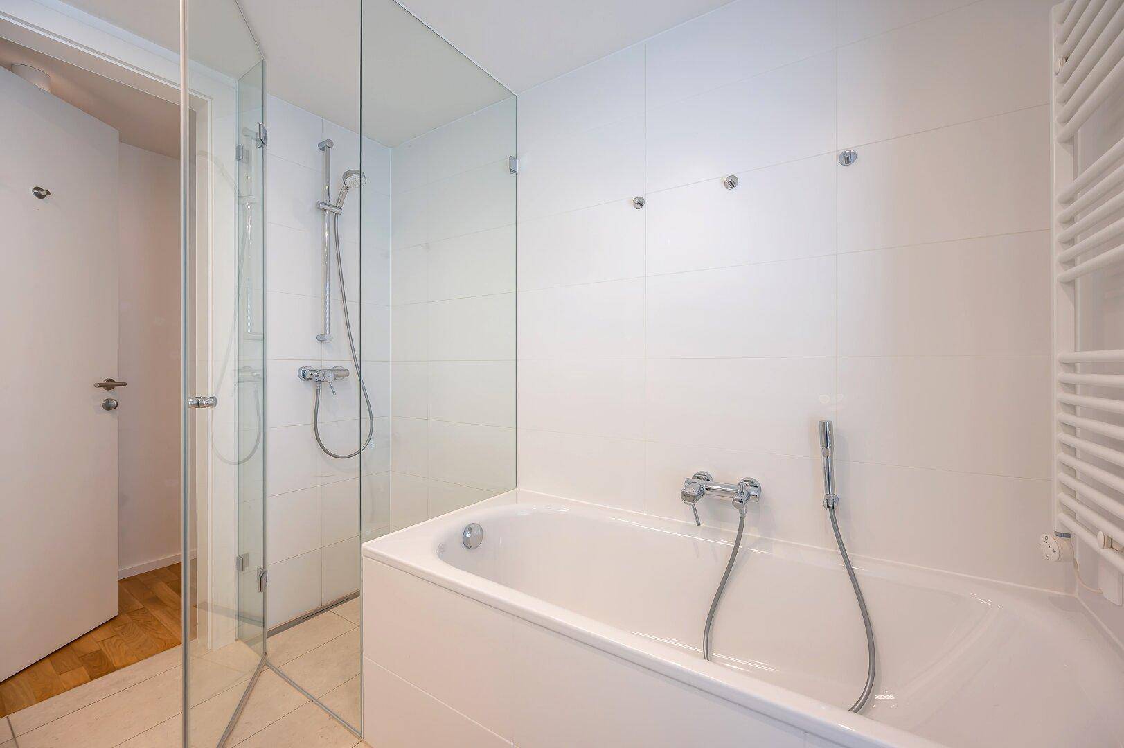 Badezimmer mit Badewanne, integrierter Dusche und beheiztem Handtuchhalter.