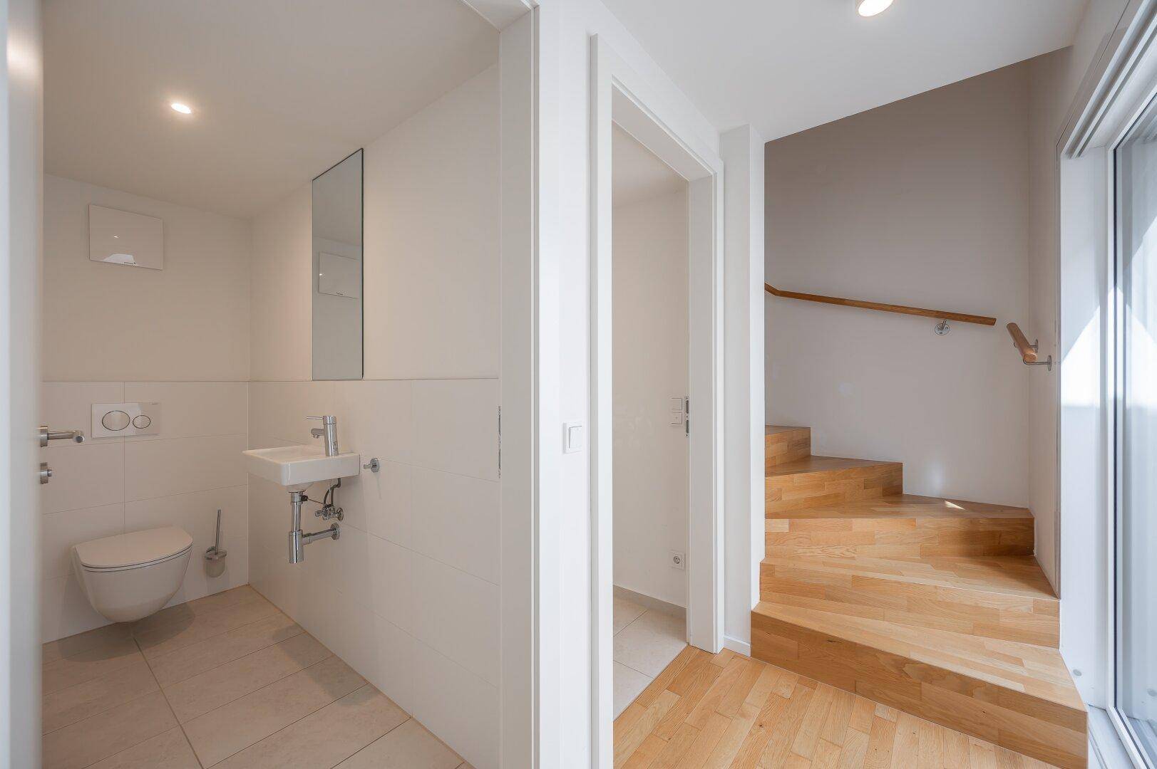 Modernes Gäste-WC mit Wand-WC, kleinem Waschbecken und hellen Fliesen.