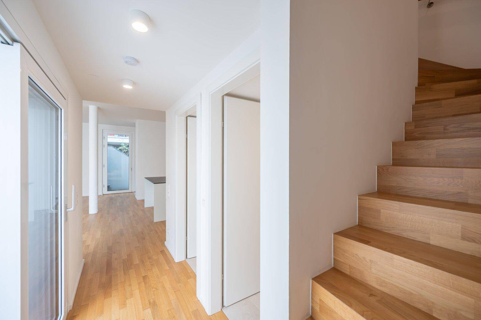Heller Flur mit Holztreppe, Holzboden und Zugang zu weiteren Räumen.
