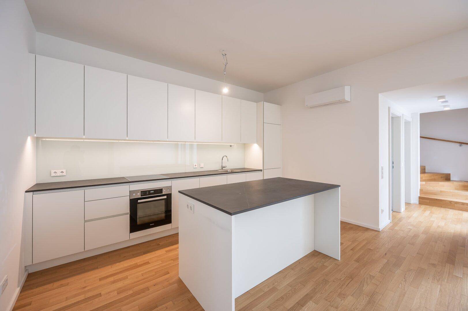 Moderne Einbauküche mit weißen Hochglanzschränken, dunkler Arbeitsplatte und Kochinsel.