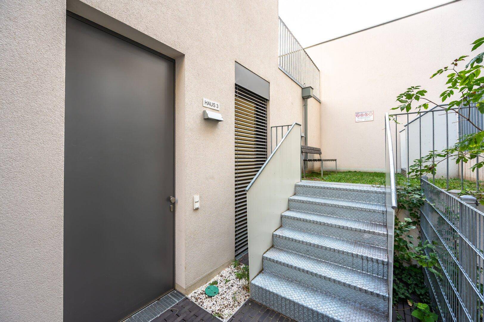 Eingangsbereich eines modernen Gebäudes mit Metalltreppe und Zugang zum Garten.