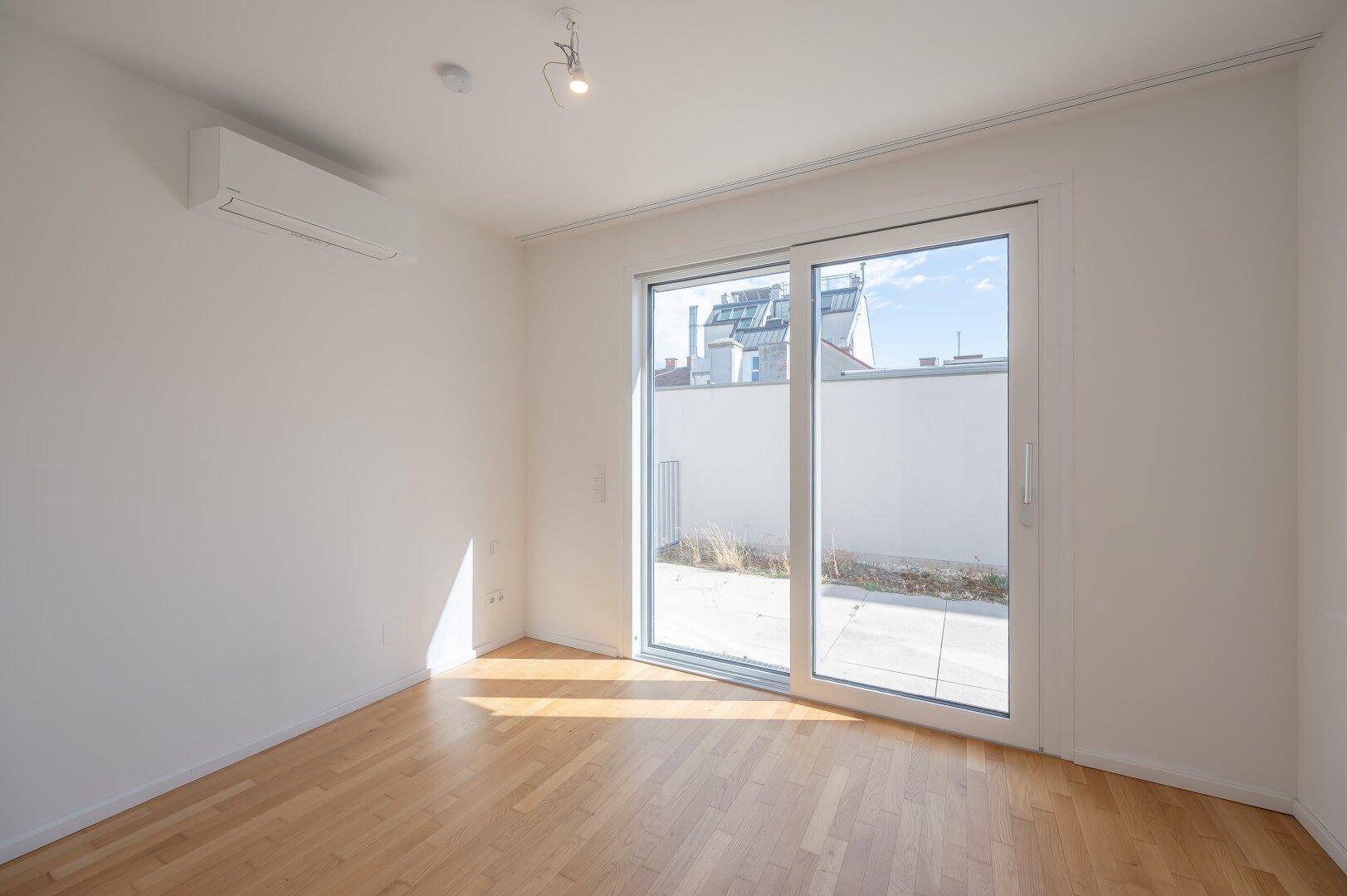 Helles Schlafzimmer mit Holzboden, Klimaanlage und Zugang zu einem Außenbereich.