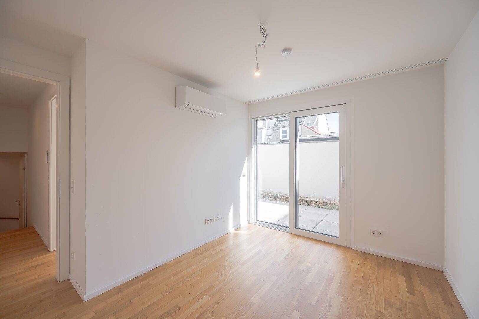 Schlafzimmer mit Holzboden, Klimaanlage und Fenster mit Blick auf den Außenbereich.