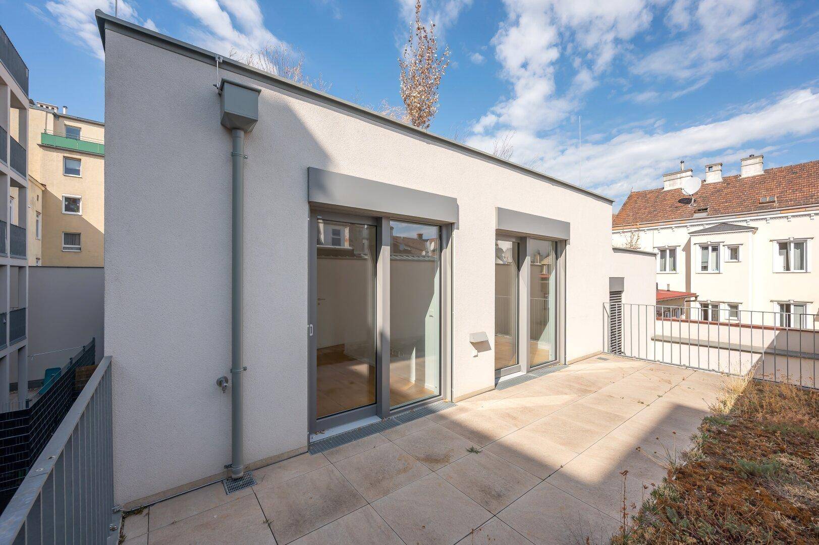 Modernes Gebäude mit Flachdach, großen Fenstern und einer Dachterrasse.
