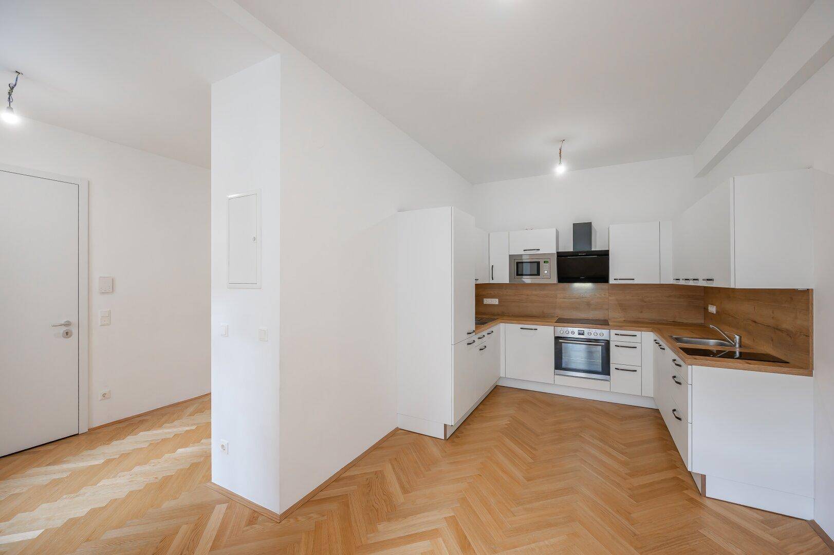 Moderne Einbauküche mit weißen Schränken, Holzarbeitsplatten und Fischgrätparkett in offenem Bereich.
