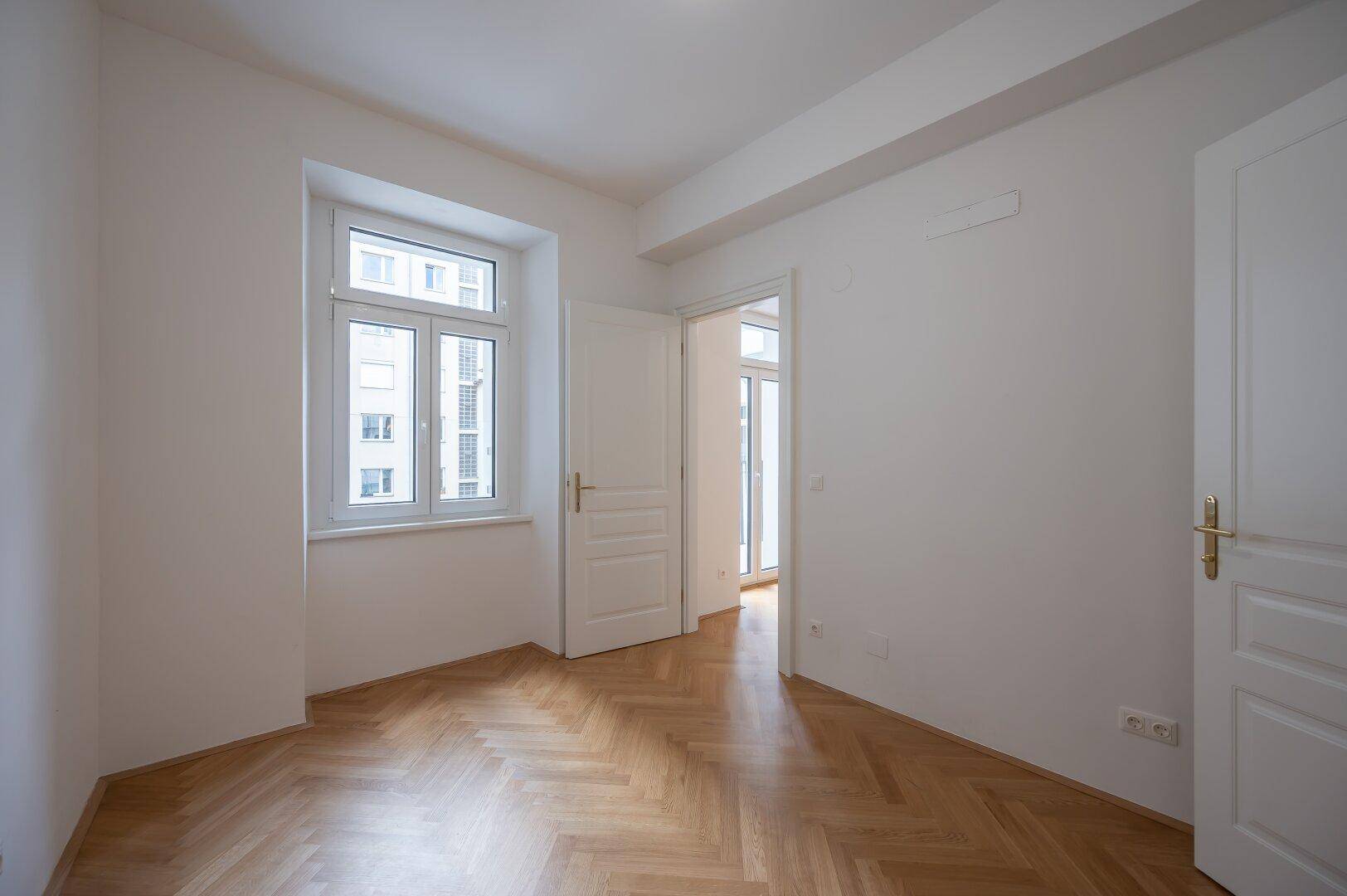 Lichtdurchflutetes Zimmer mit Fischgrätparkett und Blick auf die umliegenden Gebäude.