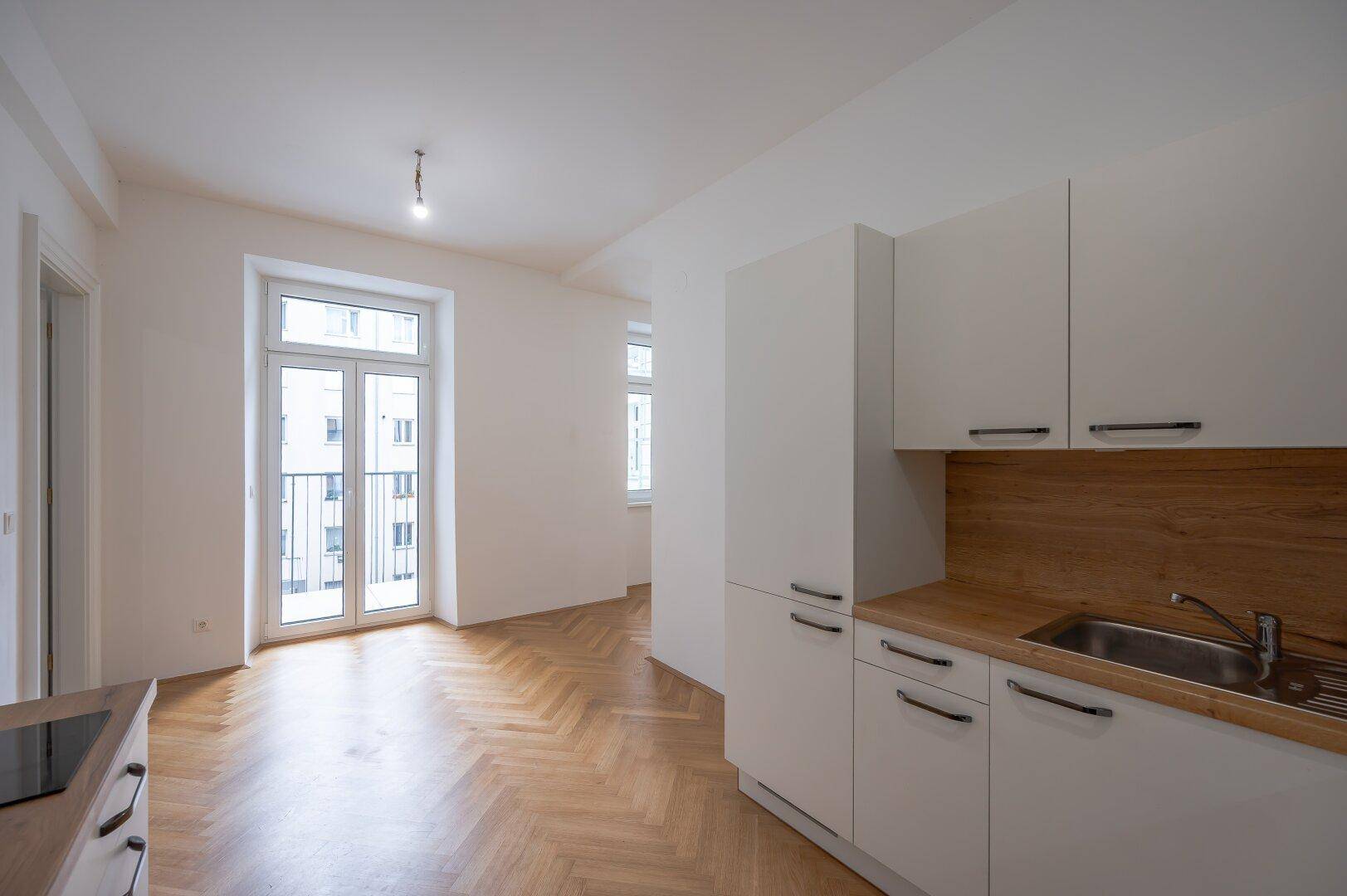 Heller Wohnbereich mit französischem Balkon und angrenzender moderner Küchenzeile.