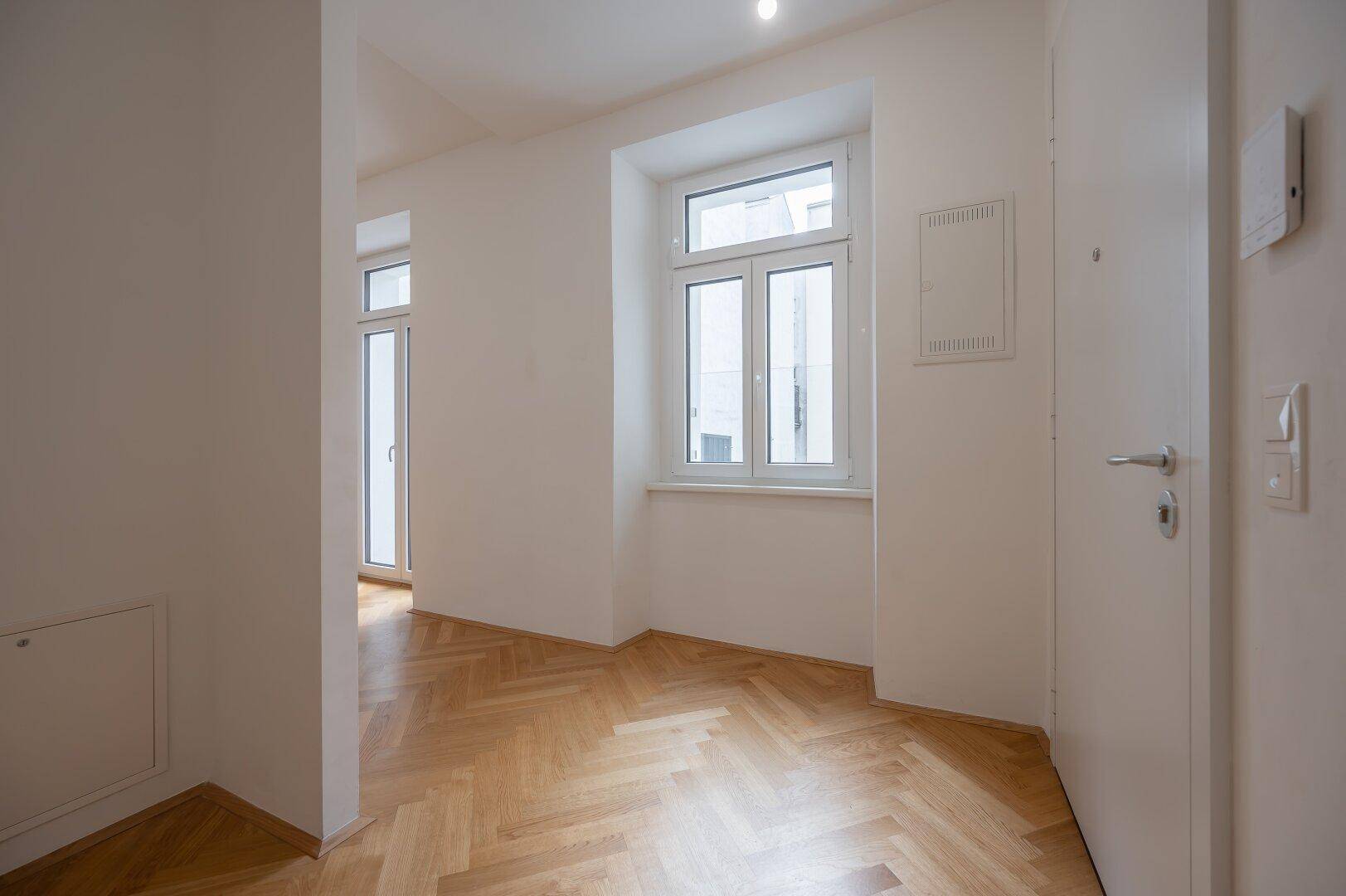 Eingangsbereich mit Fischgrätparkett, Fenster und der Wohnungseingangstür.
