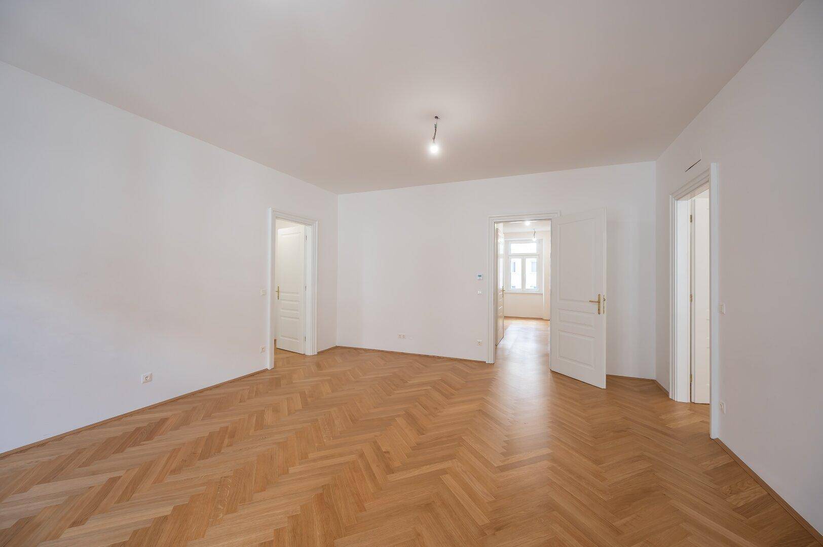 Geräumiges Zimmer mit klassischem Fischgrätparkett und mehreren Türen zu angrenzenden Räumen.