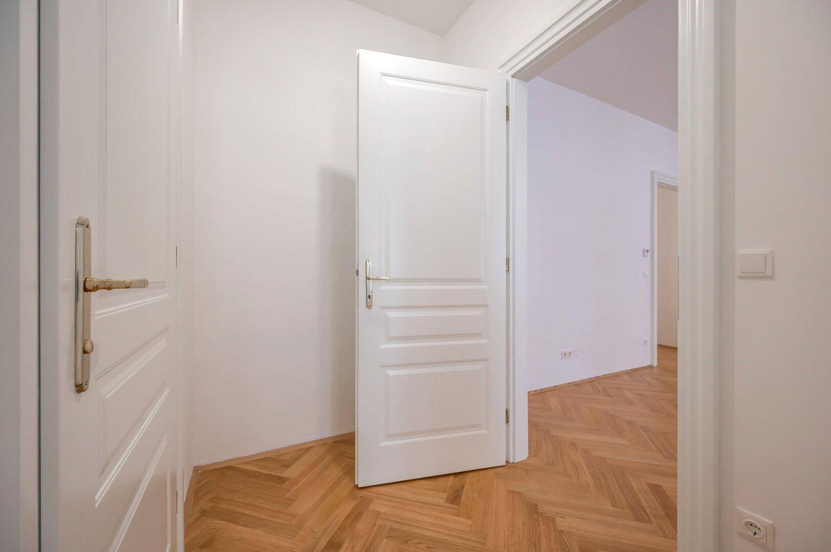 Detailansicht einer weißen Innentür im Flur mit elegantem Fischgrätparkett.