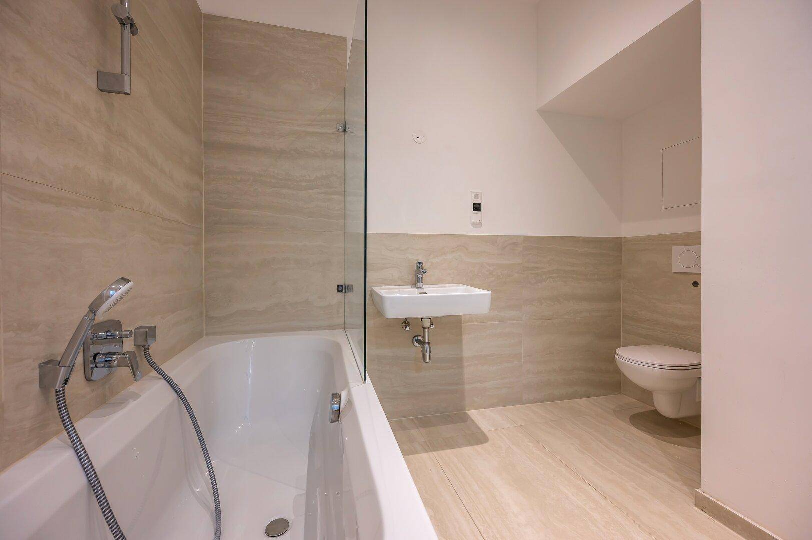 Modernes Badezimmer mit Badewanne, WC, Waschbecken und hellen Fliesen.