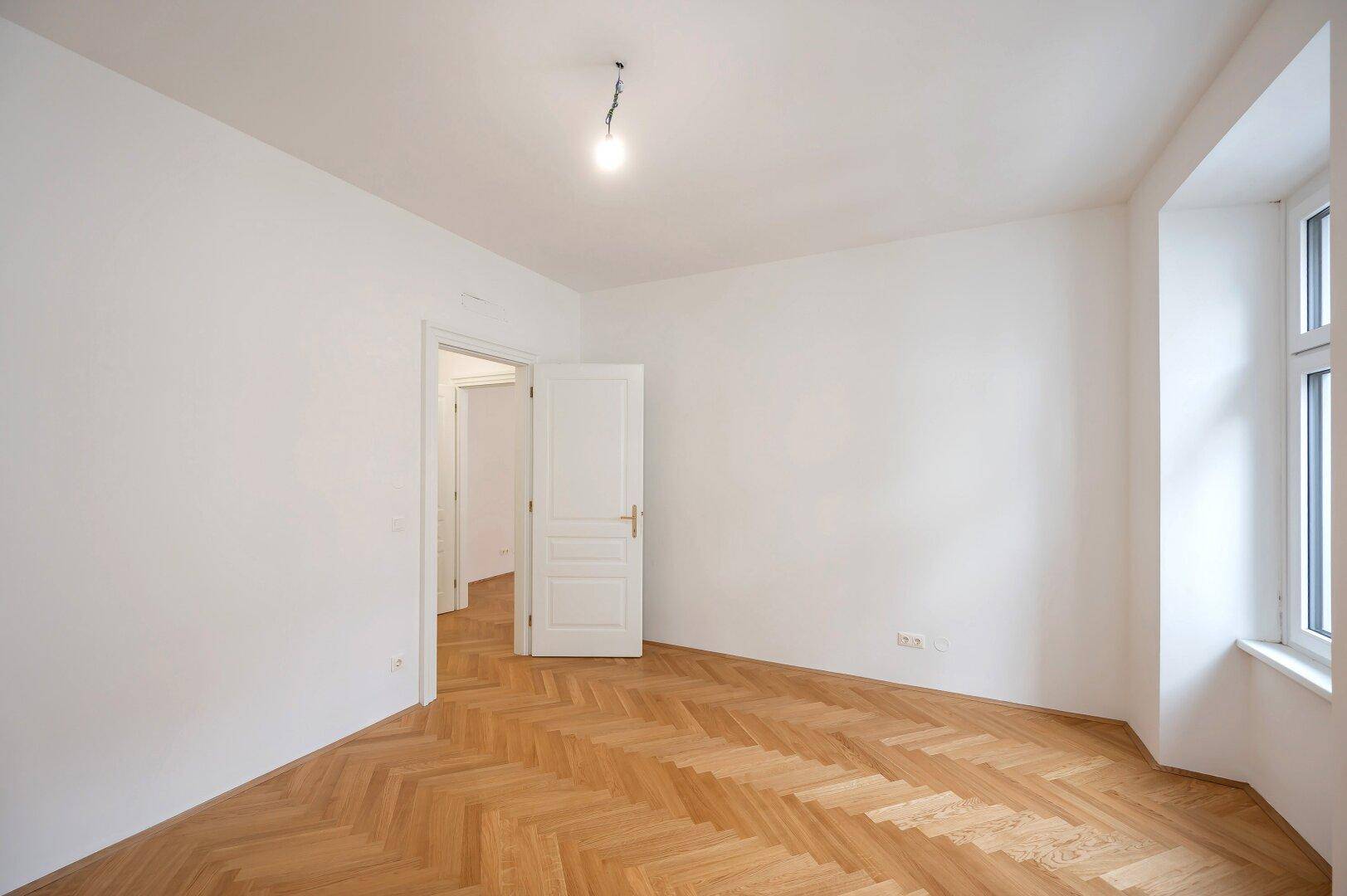 Lichtdurchflutetes Zimmer mit Fischgrätparkett und einem Fenster, das den Raum erhellt.