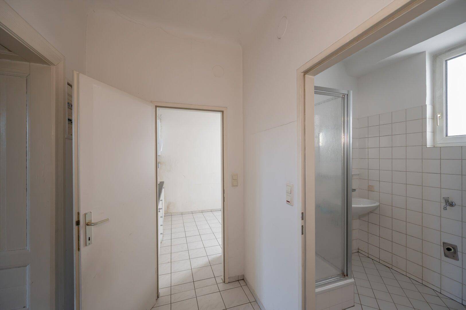 Flur mit Zugang zu einem Badezimmer und einer Küche, die beide renovierungsbedürftig sind.