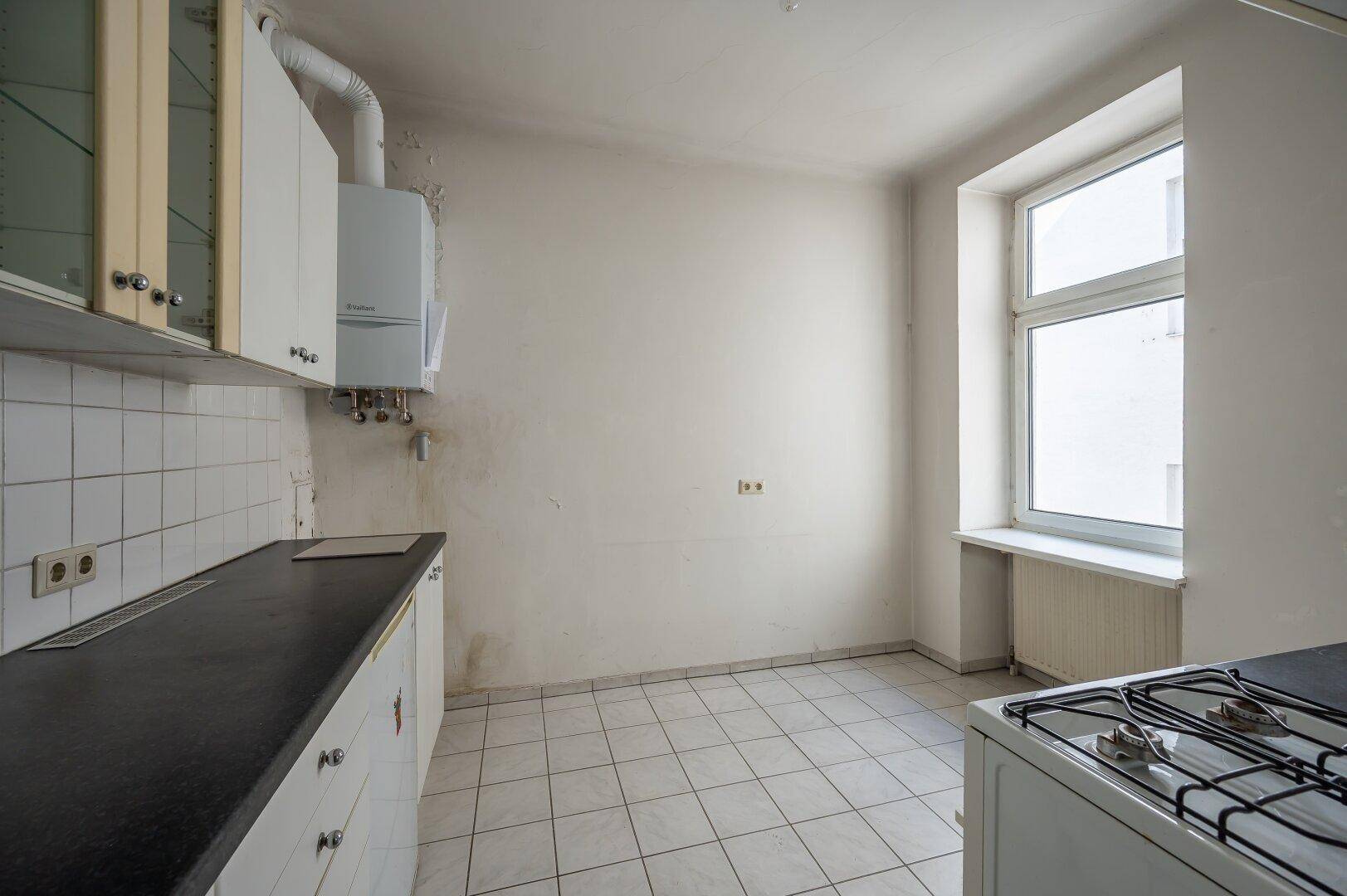Küche mit Fliesenboden, Fenster und einem Warmwasserbereiter, die auf eine Renovierung wartet.