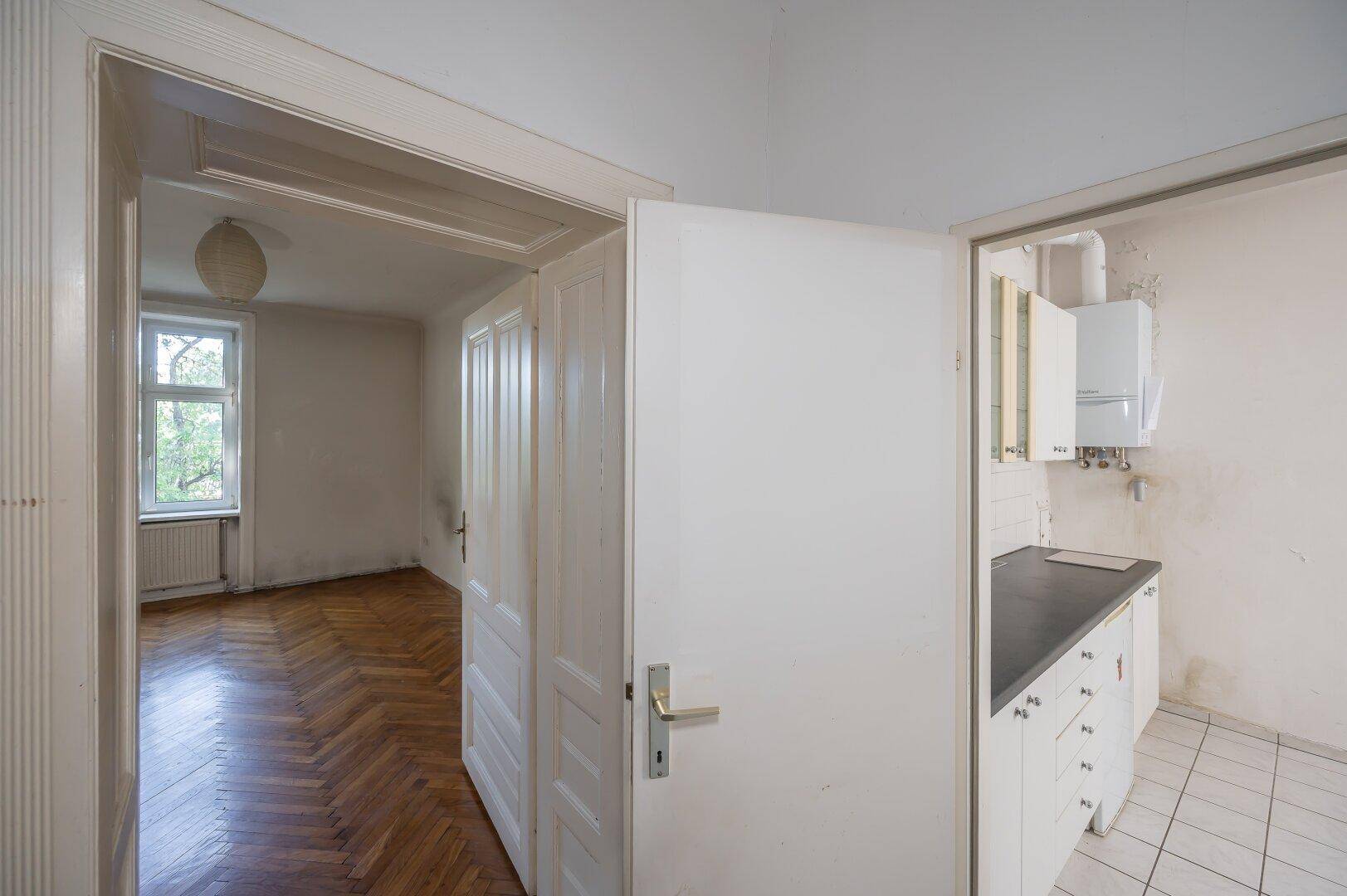 Flur mit Zugang zu einem Zimmer und einer Küche, die Renovierung benötigt.