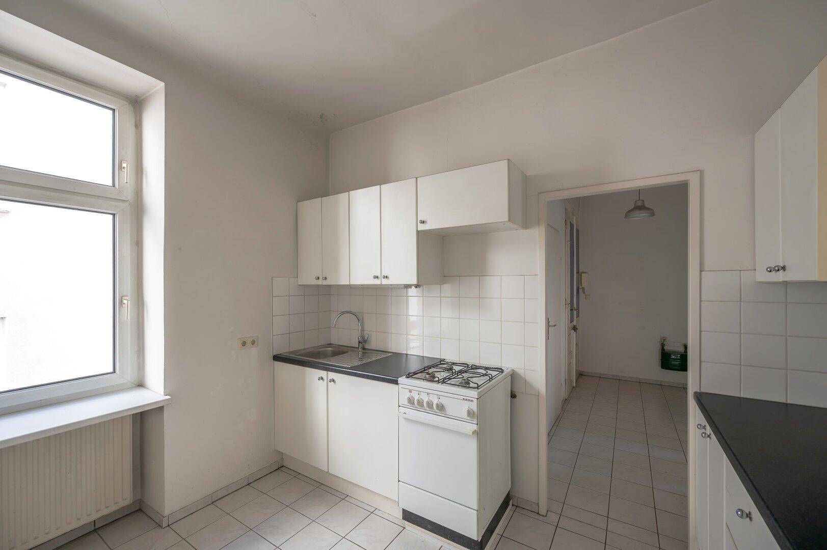 Kleine Küche mit weißen Schränken, Spüle und Gasherd, die eine Modernisierung benötigt.