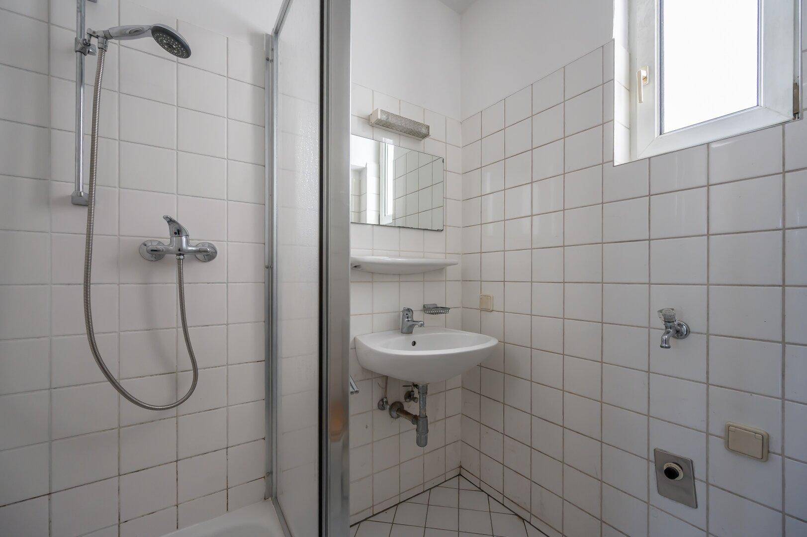 Badezimmer mit Duschkabine, Waschbecken und weißen Fliesen, das einfach ausgestattet ist.
