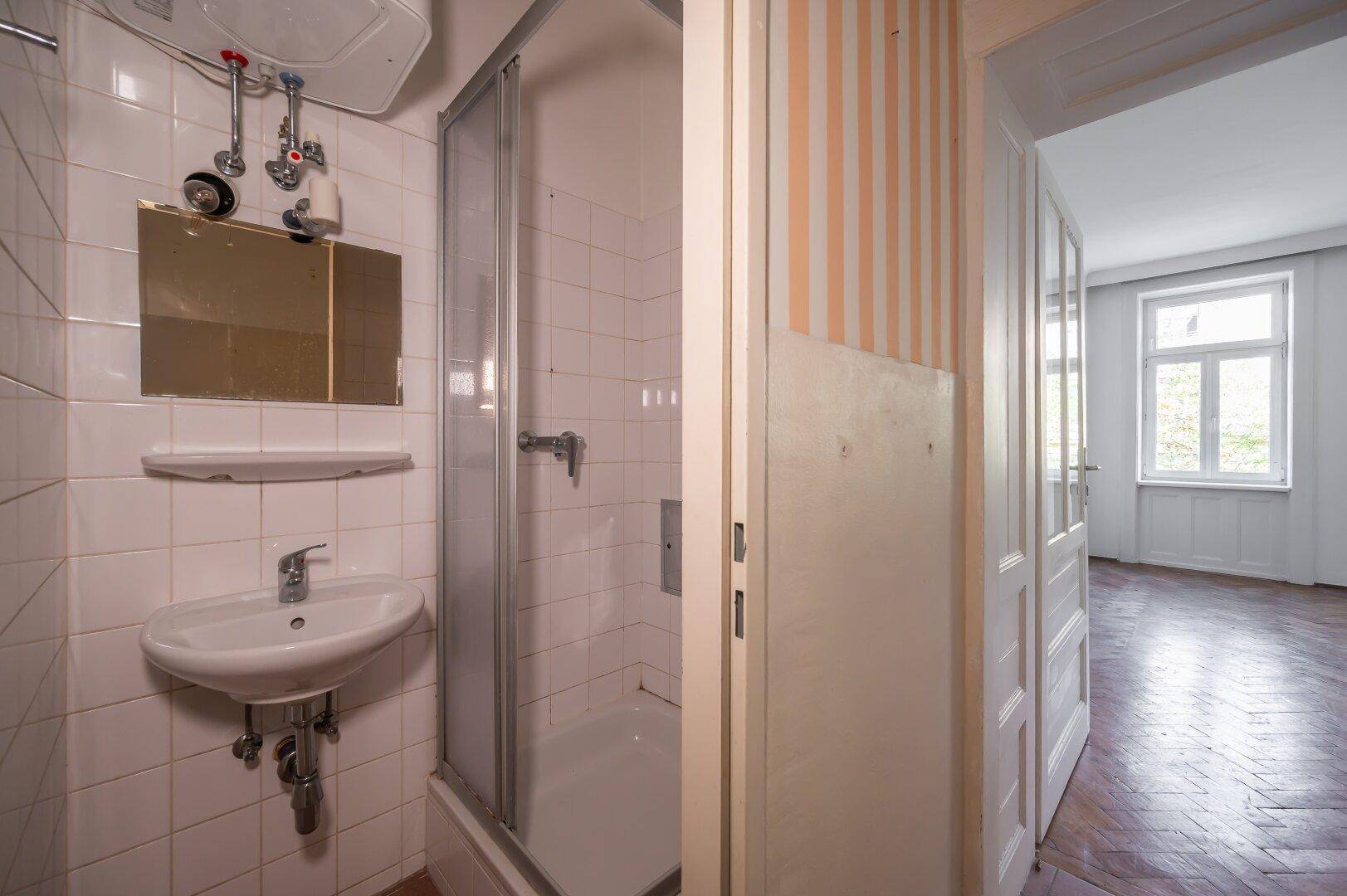 Kleines Badezimmer mit Duschkabine, Waschbecken und weißen Wandfliesen.