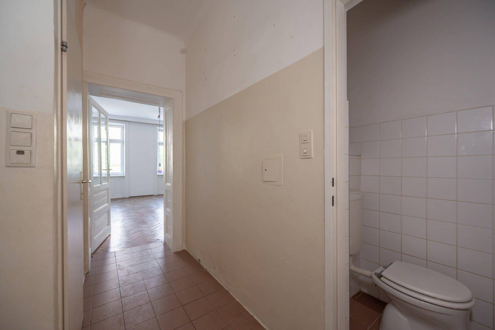 Flur mit Fliesenboden und Zugang zu einem separaten WC, der zu weiteren Räumen führt.