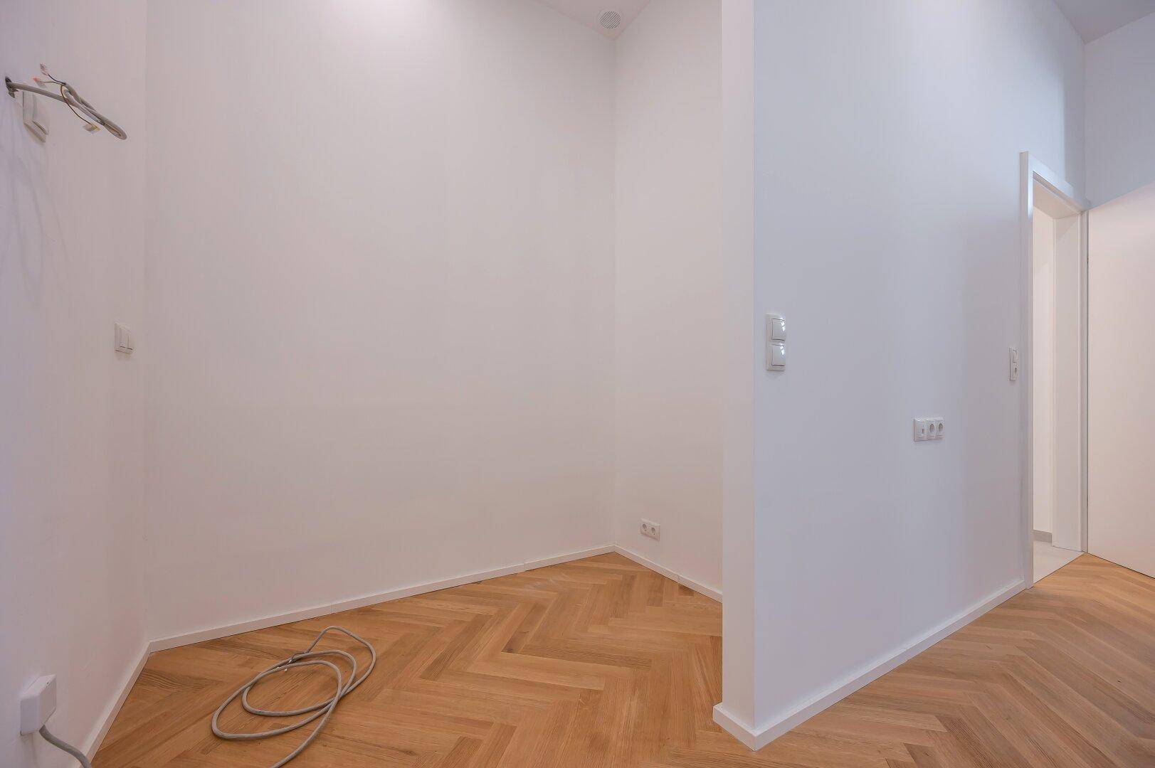 Leerer Raum mit Fischgrätparkett und Anschlüssen, ideal als Hauswirtschafts- oder Abstellraum.