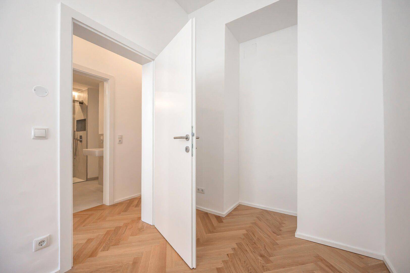 Heller Flur mit Fischgrätparkett, der zu einem modernen Badezimmer mit Dusche führt.