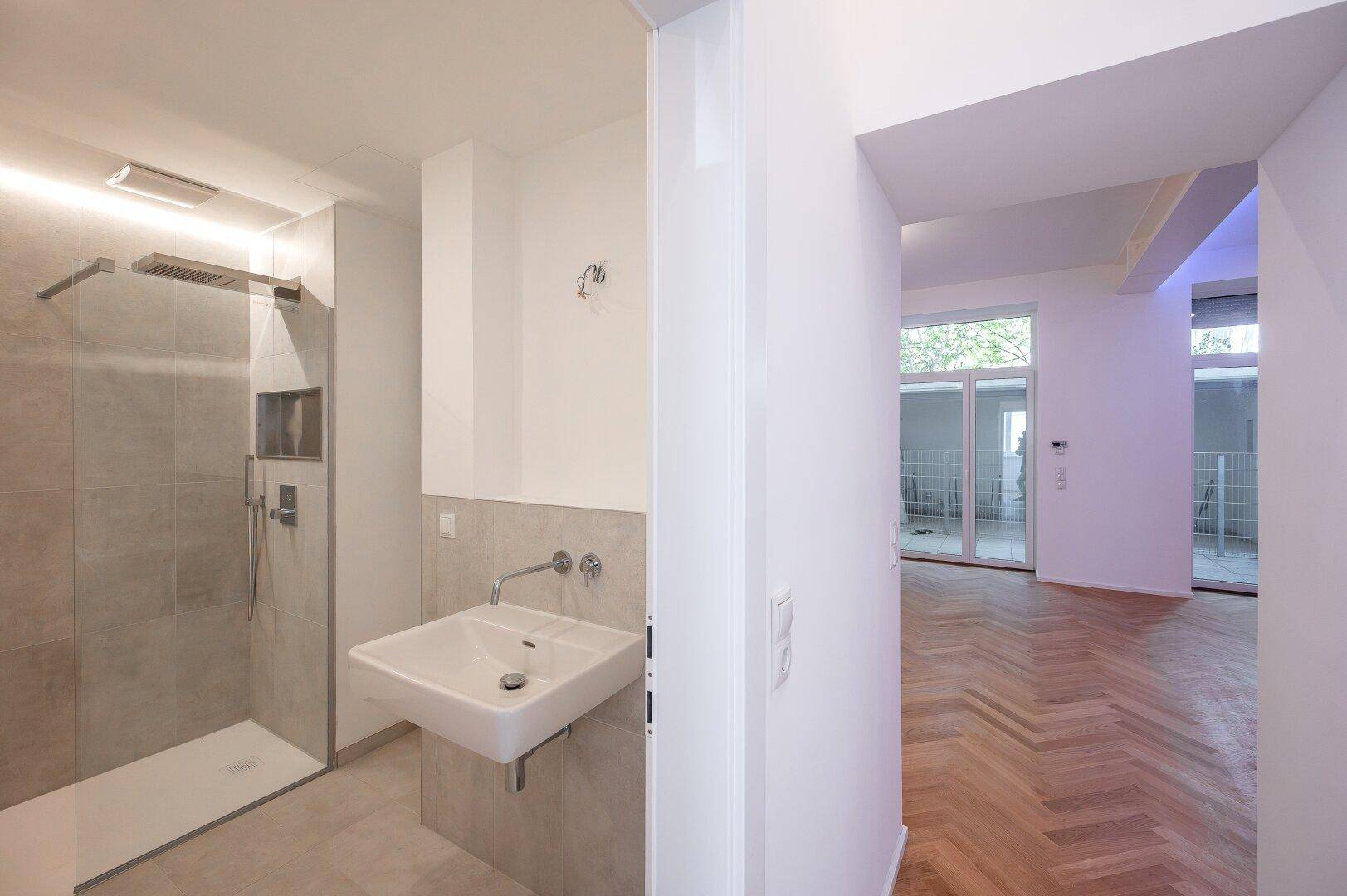 Modernes Badezimmer mit begehbarer Dusche und Waschbecken, mit Blick in den hellen Wohnbereich.