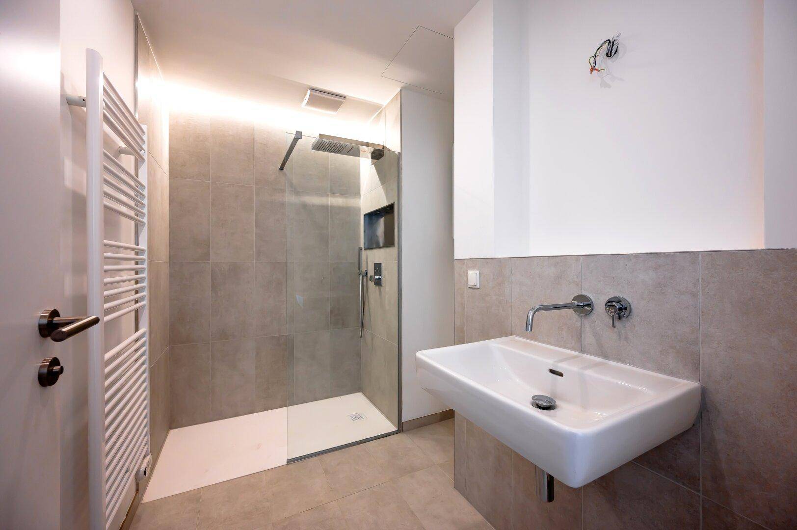Elegantes Badezimmer mit großer begehbarer Dusche, Regenduschkopf und beheiztem Handtuchhalter.