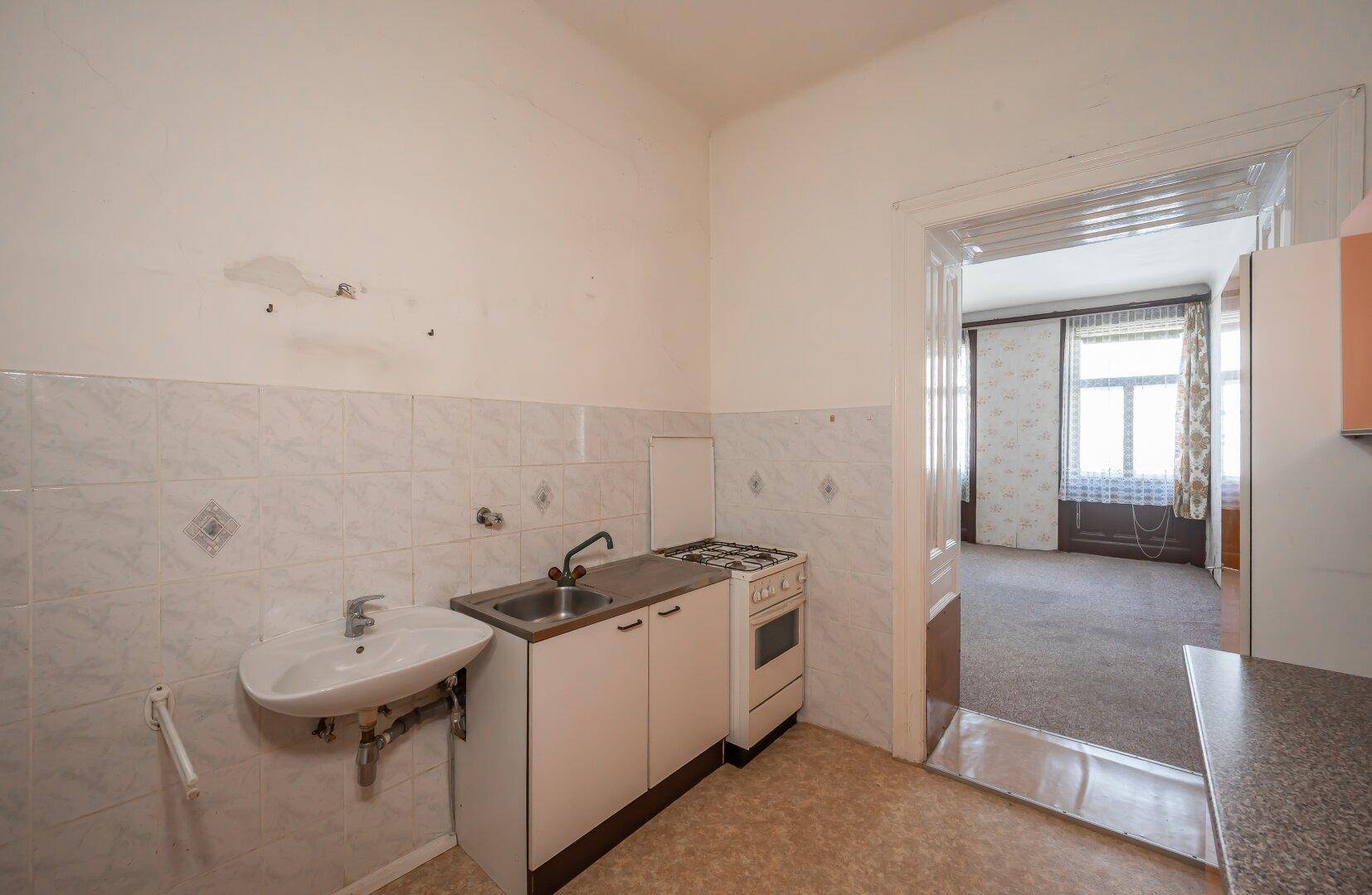 Küche mit Gasherd und Spüle, mit Blick durch die offene Tür in das angrenzende Zimmer.