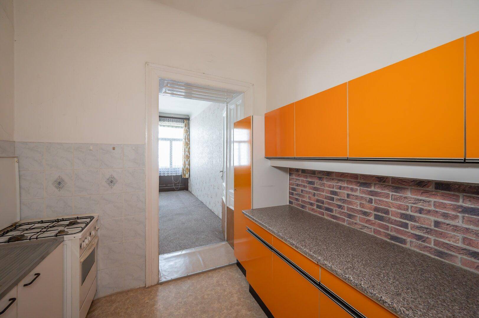 Küche mit Gasherd und Blick in das angrenzende Zimmer, das eine Renovierung benötigt.