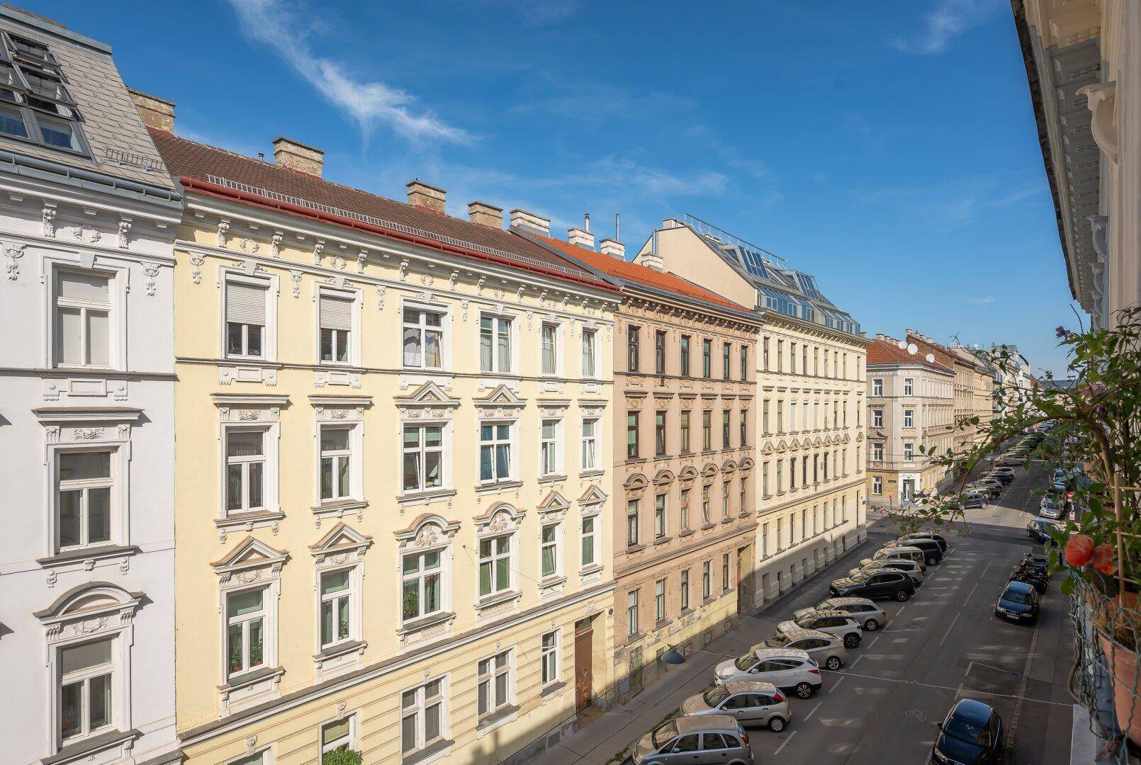 Weitläufiger Blick auf eine städtische Straße mit historischen Wohngebäuden unter blauem Himmel.