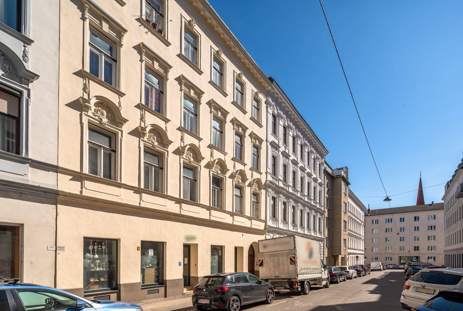 Straßenansicht eines historischen Wohngebäudes mit geparkten Autos und klarem Himmel.
