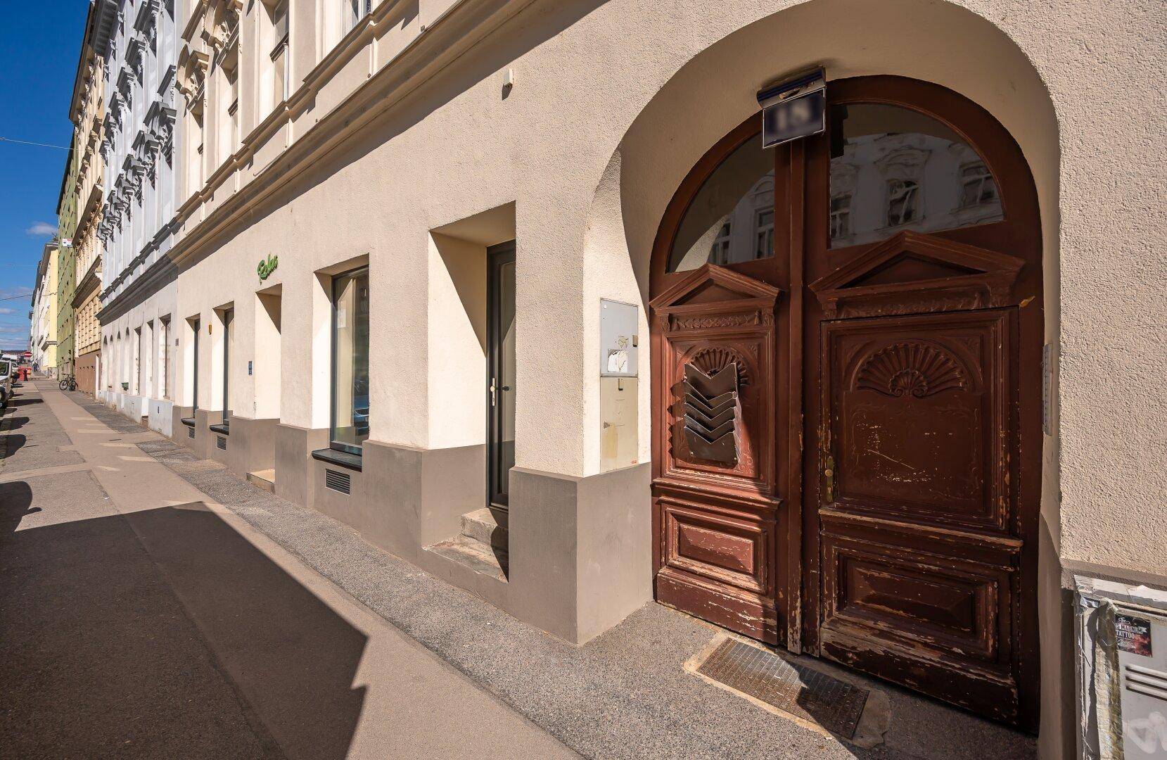 Historischer Gebäudeeingang mit großer, verzierter Holztür und Bogenarchitektur von der Straße aus gesehen.