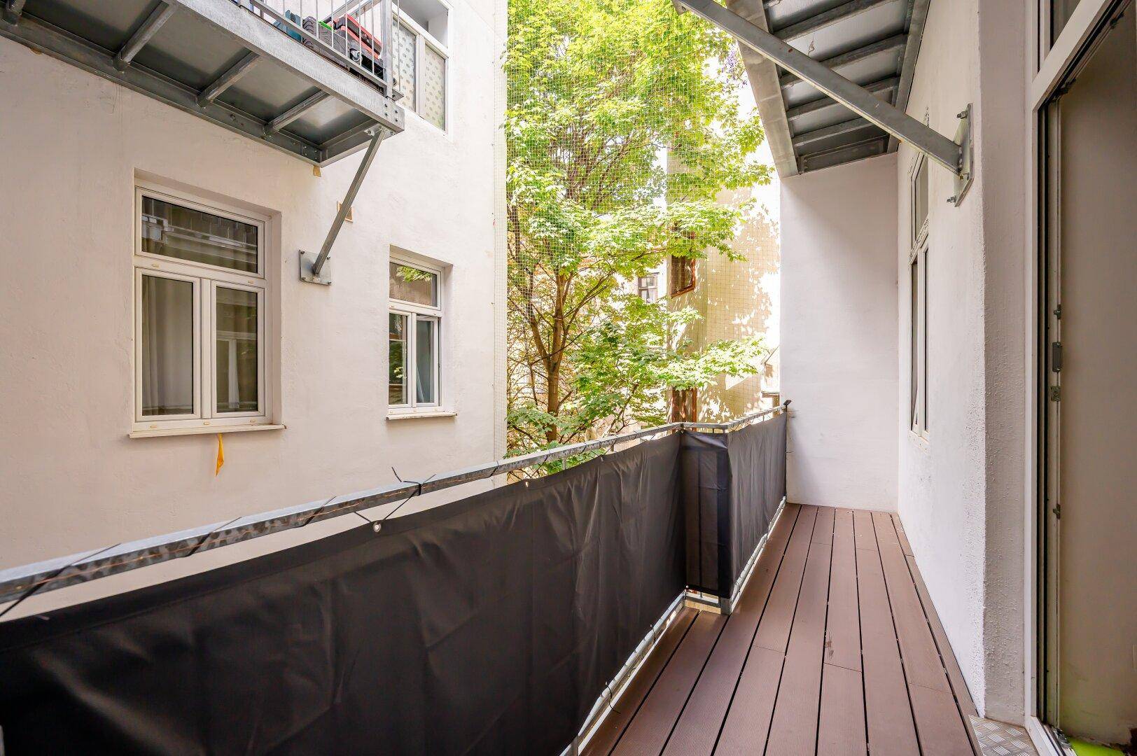 Schmaler Balkon mit Holzboden und schwarzem Sichtschutz, bietet einen Blick in den Innenhof.