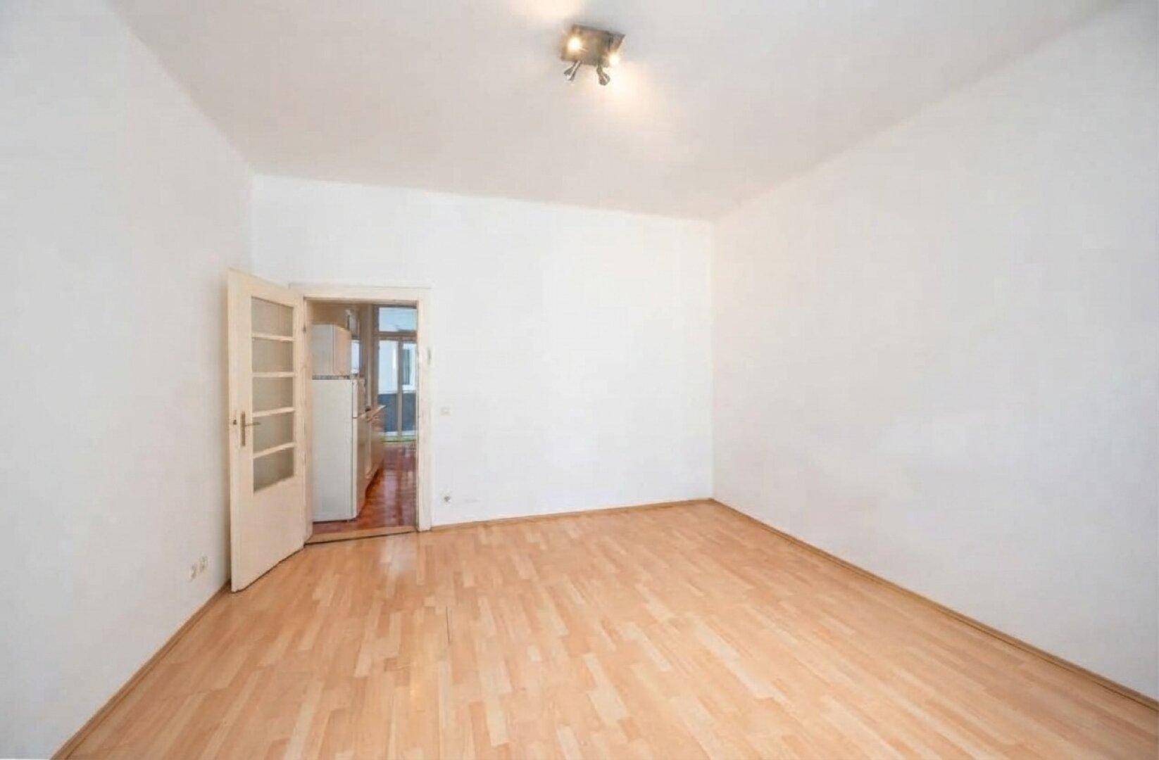 Geräumiges Wohnzimmer mit Parkettboden und Zugang zu einem weiteren Raum.