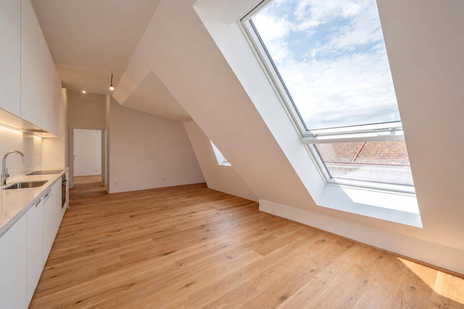 Moderne Küchenzeile im Dachgeschoss mit Holzboden, Dachfenstern und viel natürlichem Licht.