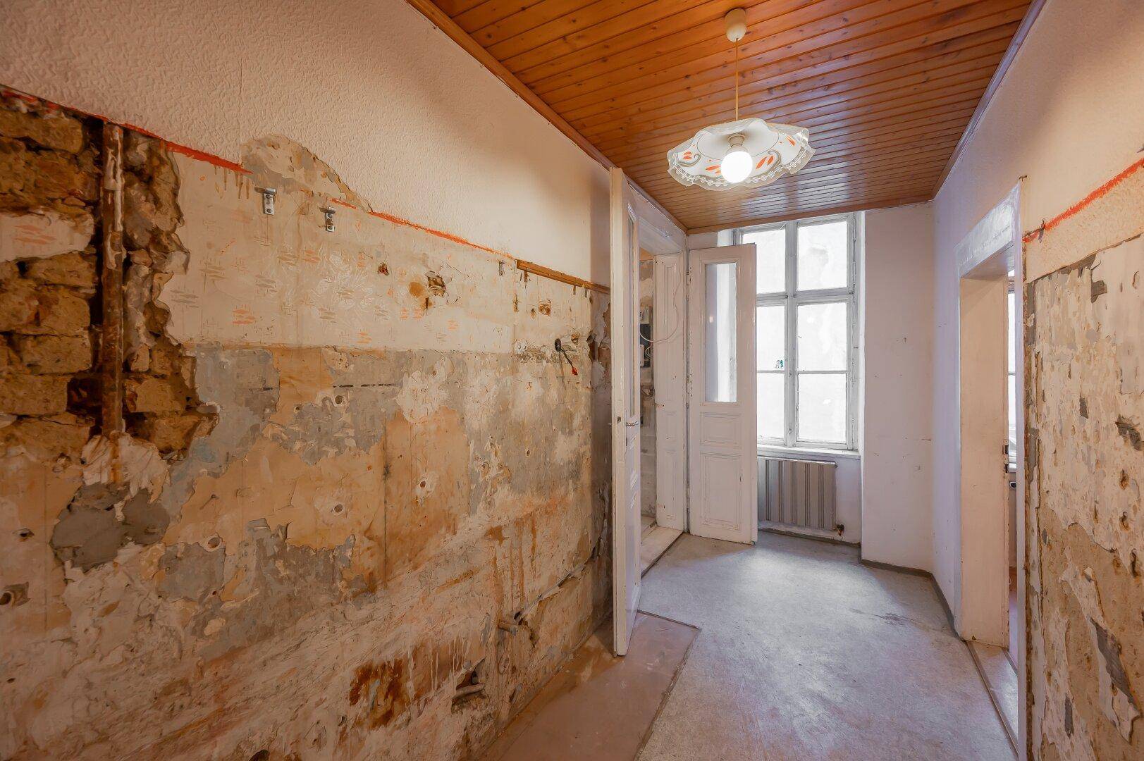 Langer Flur mit freigelegten Wänden und Holzdecke, der auf eine umfassende Renovierung wartet.