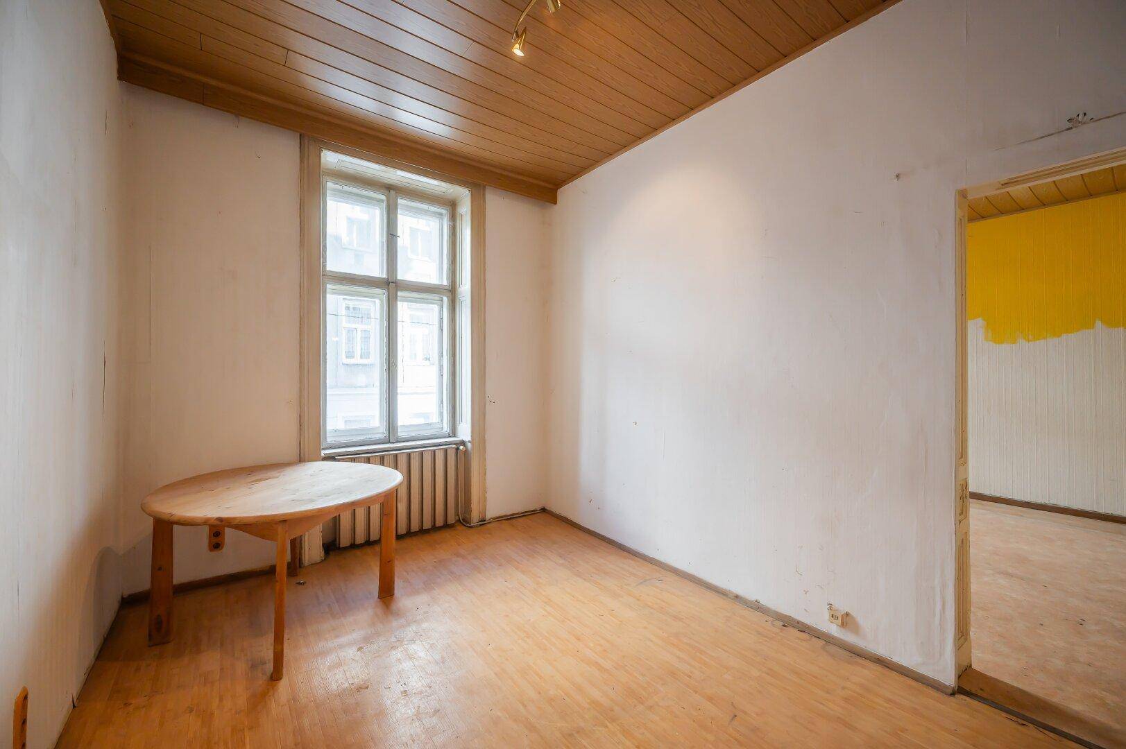Kleiner Raum mit Holztisch, Parkettboden und einem Fenster, ideal für ein Esszimmer oder Büro.