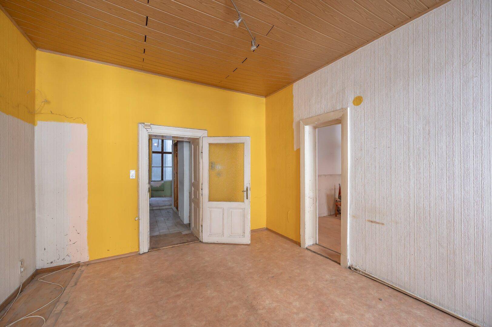 Heller Raum mit gelben Wänden, Holzdecke und mehreren Türen, ideal für eine Neugestaltung.