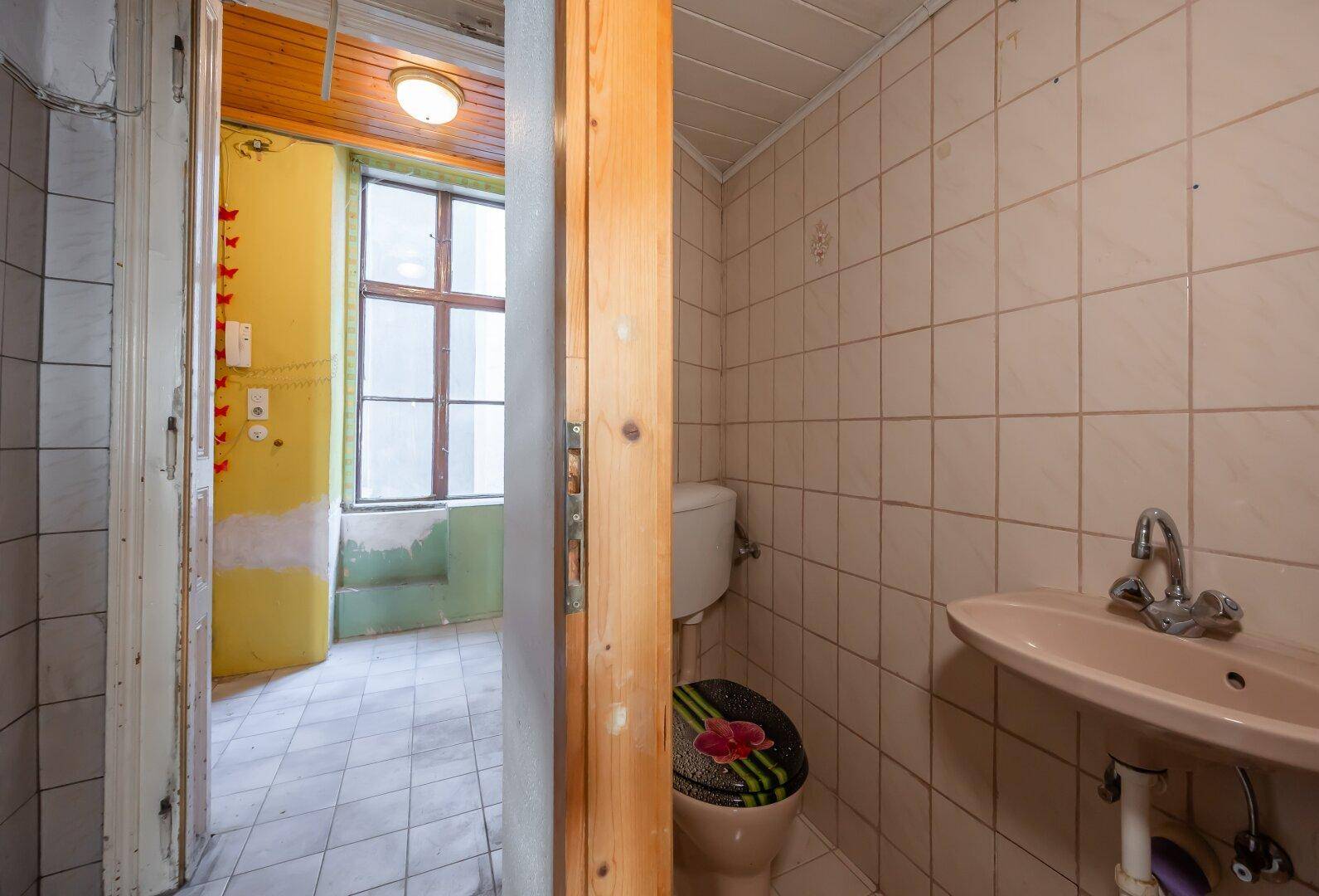 Kleines WC mit beigefarbenen Fliesen, Toilette und Waschbecken, in originalem Zustand.