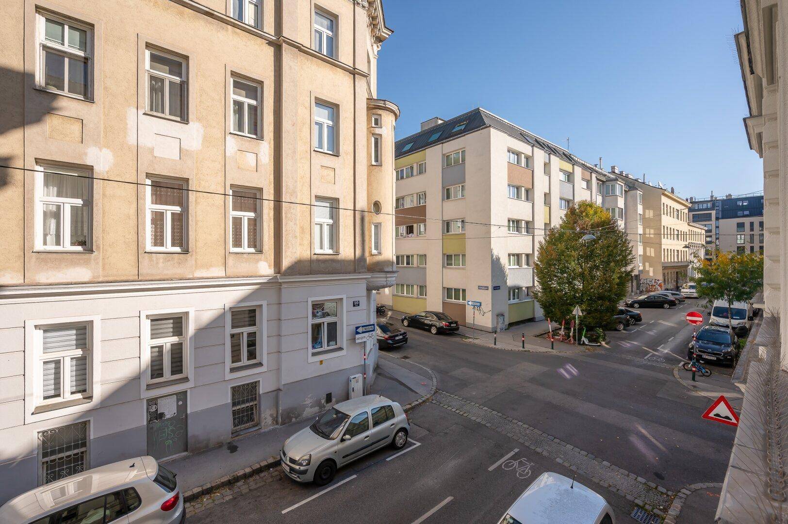 Blick auf eine belebte Stadtstraße mit parkenden Autos und verschiedenen Wohngebäuden.