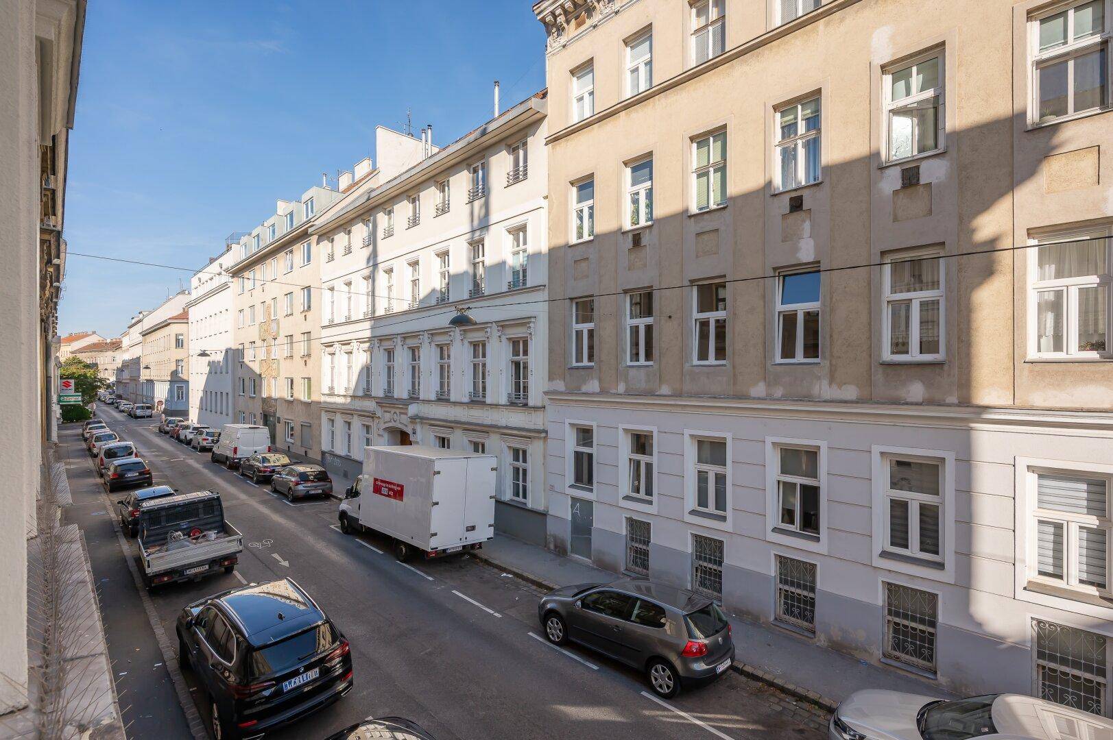 Panoramablick auf eine städtische Straße mit parkenden Autos und historischen Gebäuden.