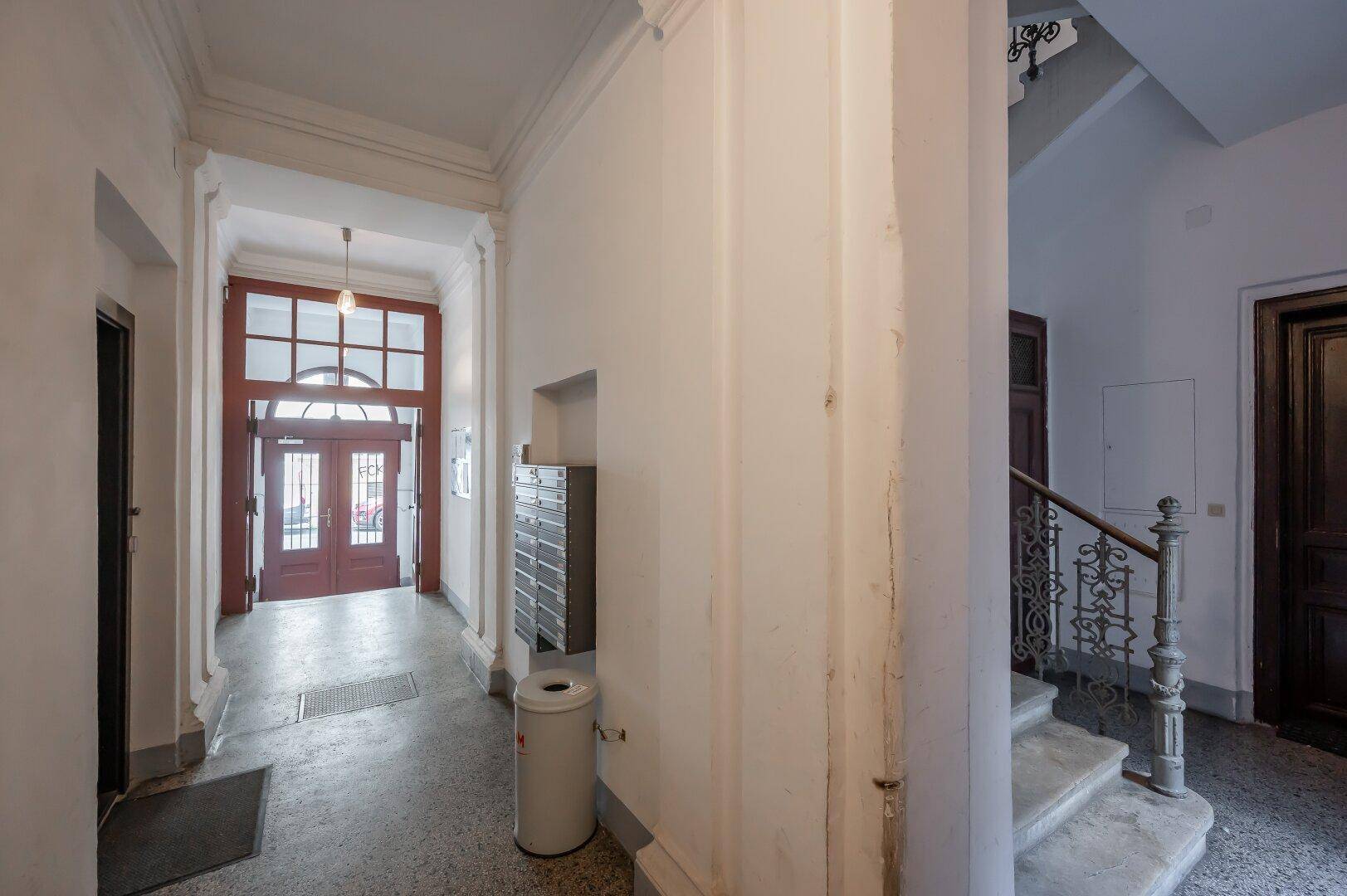 Heller Eingangsbereich eines Altbaus mit Terrazzoboden und Treppenaufgang, der zum Lift führt.