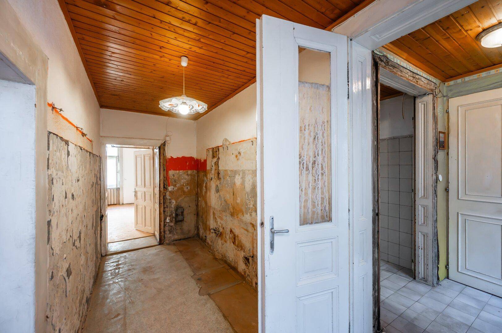 Langer Flur mit freigelegten Wänden und Holzdecke, der auf eine umfassende Renovierung wartet.