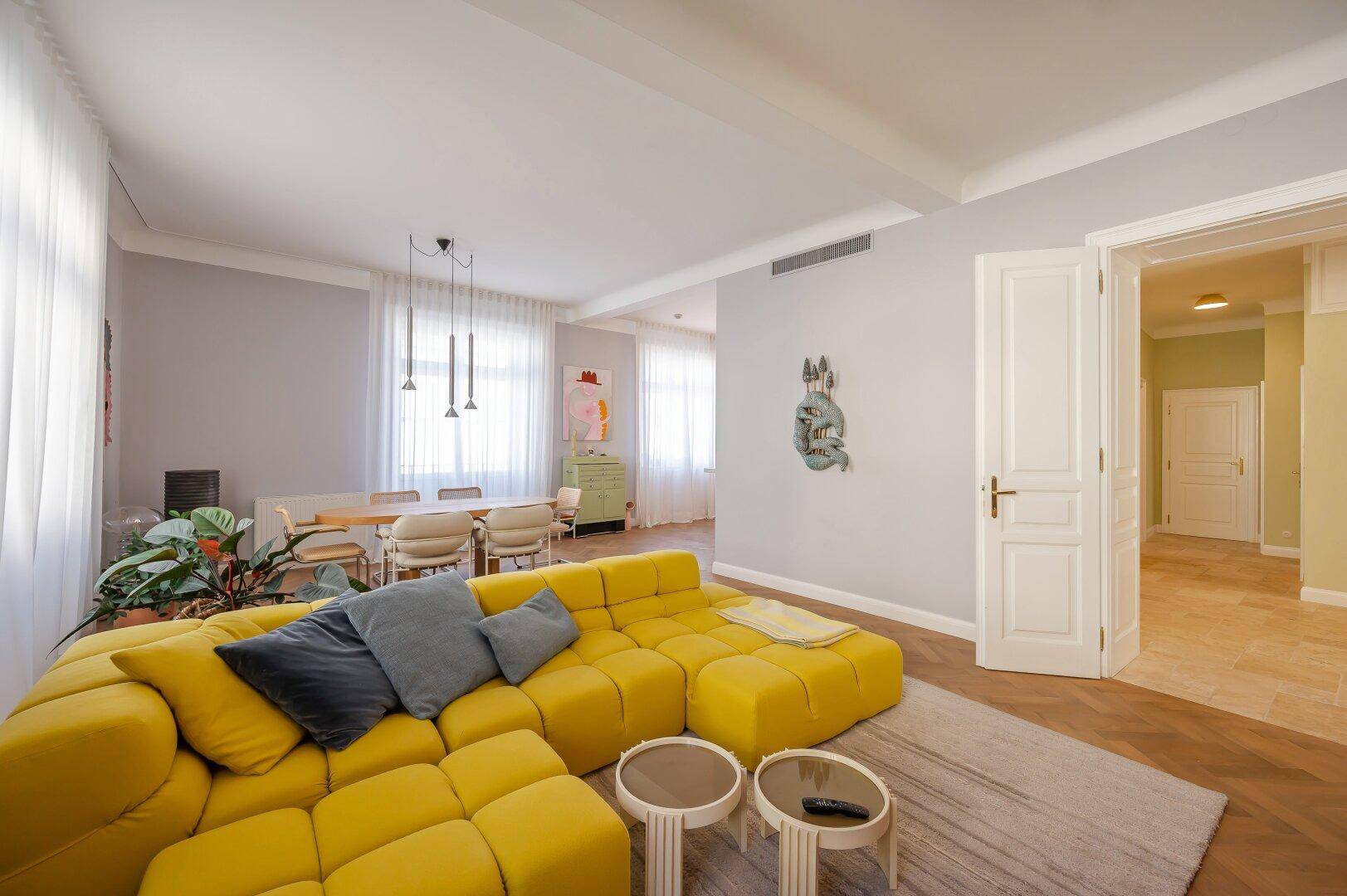 Geräumiger Wohnbereich mit modernem gelbem Sofa, Parkettboden und Blick in den Flur.