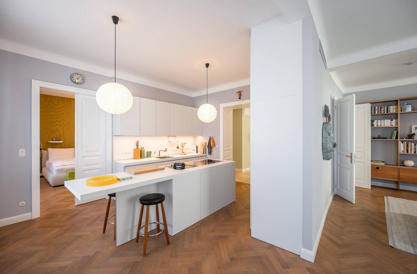 Moderne Küche mit Kochinsel und Frühstücksbar, offen zum Wohnbereich und Flur.