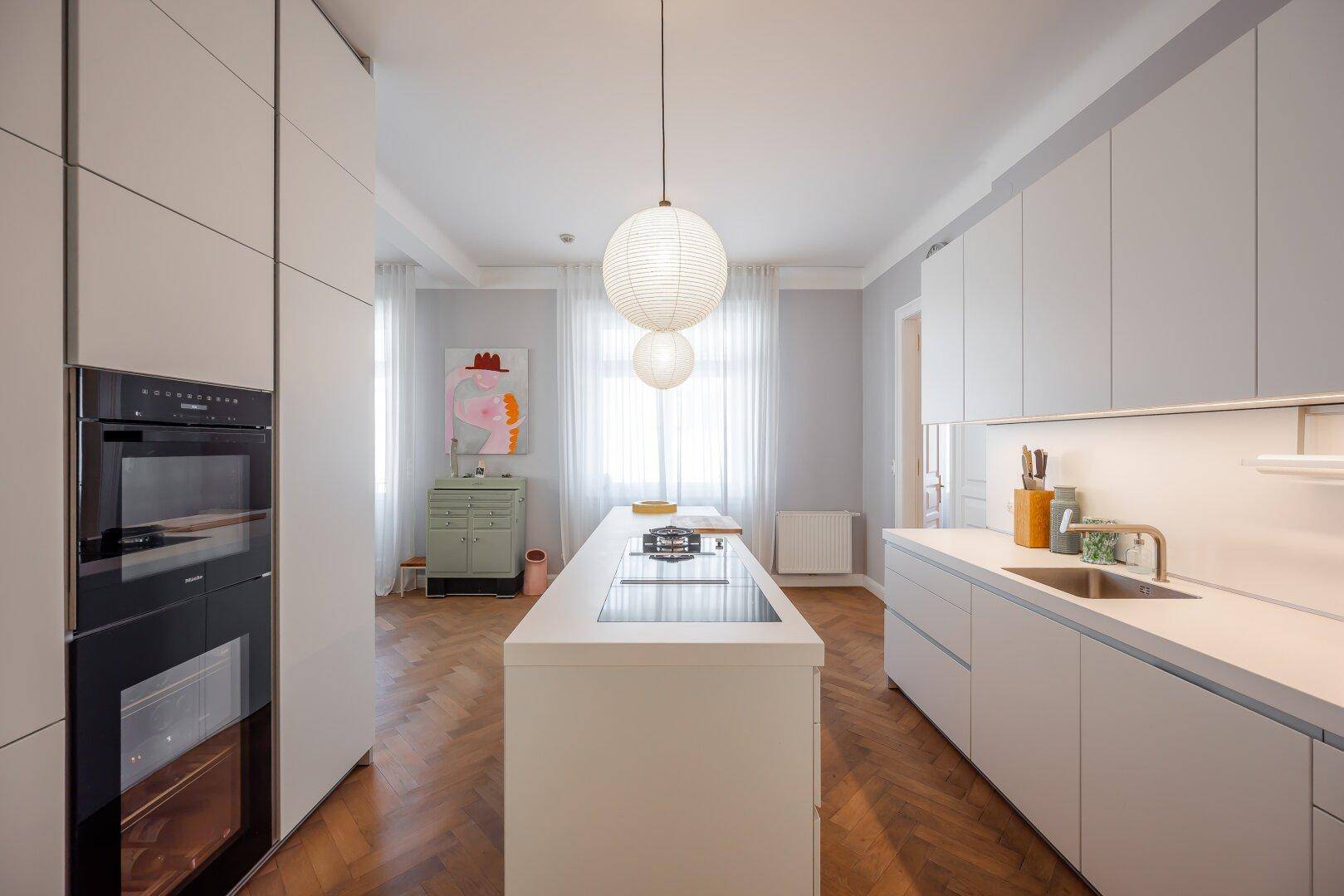 Elegante weiße Küche mit Kochinsel, integriertem Backofen und Blick auf den Wohnbereich.